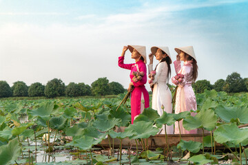 Elegant Trio on Water: Three women gracefully navigate a boat amidst a sea of lily pads, their traditional conical hats and vibrant attire adding a splash of color to the serene water landscape.