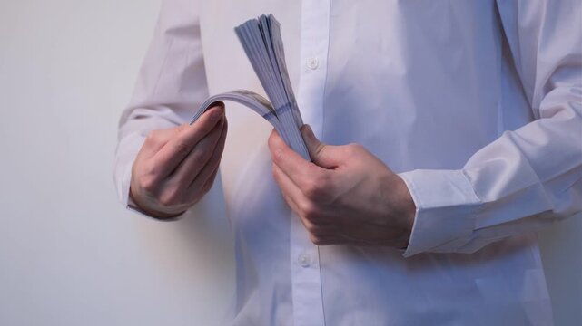 Young man in white shirt on white background flipping through thick stack of dollar bills