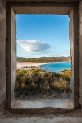Fototapeta premium Beach and sea view framed by a glassless window in an abandoned house in Villasimius, Sardinia, Italy