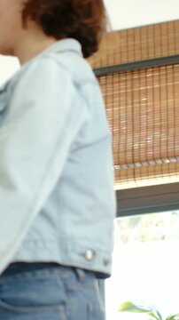 Vertical video: Smiling raising arm woman in denim walking kitchen taking friend's hand to dance