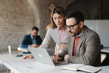  Professional manager showing data on a laptop to his colleagues in a modern office.