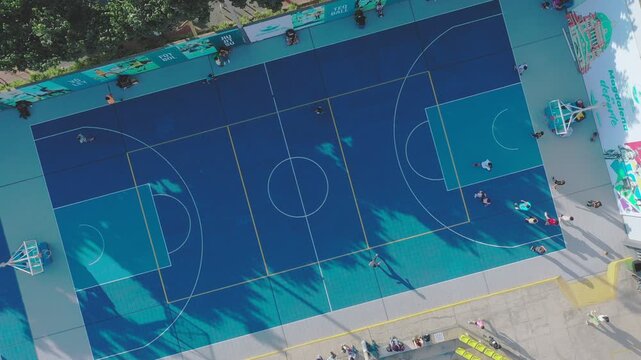 Aerial view of people playing basketball on a modern blue and gray court with shadows