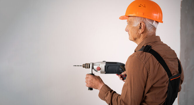 Focused Senior elderly builder using electric drill perforator during building construction or renovation. construction professional at work