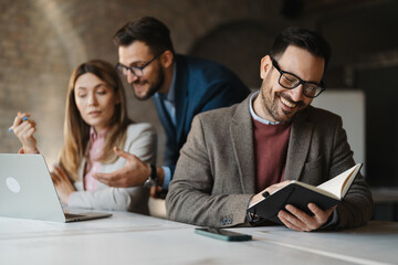 Focused manager checking his planner or agenda while working at a desk in a busy open-space office.