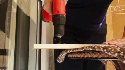Woman drilling a hole in a wooden board using a small power drill at home. Horizontal video ideal for household tools, DIY,  home renovation, and residential maintenance content. - Powered by Adobe