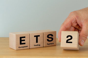 ETS 2 European Trading System. Business, environmental concept. Text ETS on wooden blocks and a businessman's hand adding a cube with the number two. New System for Trading in Carbon Emission Permits.