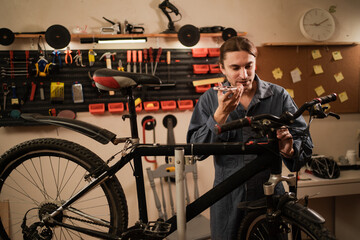 Professional mechanic recording voice message on smartphone while repairing bicycle and consulting with AI.