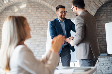 Two business professionals shaking hands after a successful deal in a modern, sunlit office.
