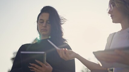 A group of young students engaged in an insightful discussion, collaborating on a project outdoors under the bright sun. They share ideas, take notes, and utilize technology for modern learning. - Powered by Adobe
