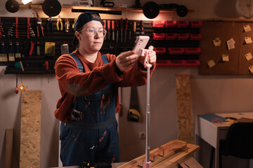 Female carpenter in workshop recording video blog for social media using smartphone