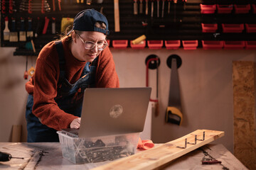 Female small business owner using laptop at her workplace in carpentry workshop in evening