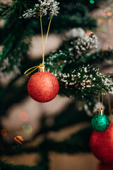Shiny red and green Christmas tree balls, decorations hanging from dark green branches, create a...