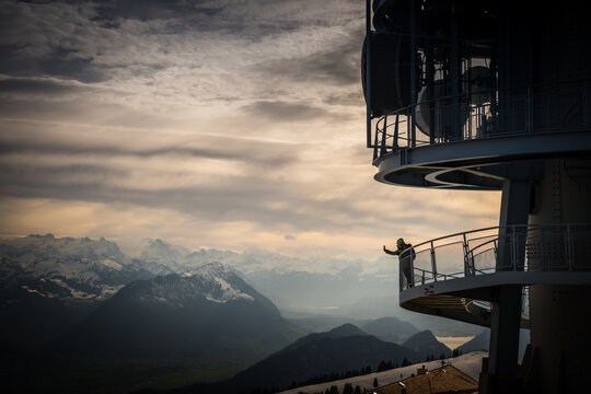 View of a person with arms outstretched on the observation deck of a communications tower with snow-capped mountains in the distance, Lucerne, Canton Lucerne, Switzerland.