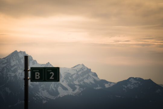 View of snow-capped mountain peaks under a cloudy sky, with a green signpost in the foreground, creating a serene alpine vista, Lucerne, Canton Lucerne, Switzerland.