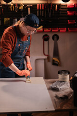 Female carpenter working with old furniture painting table top in garage or small workshop.