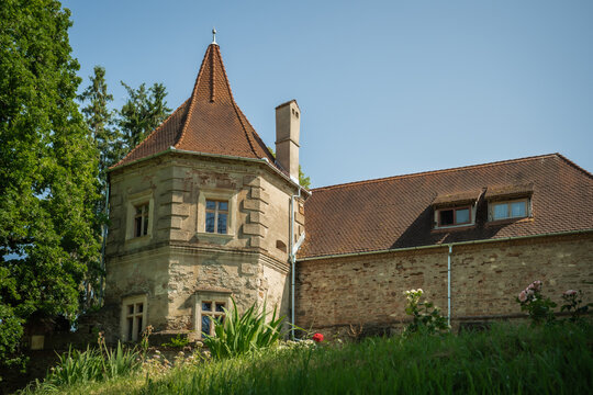 View of the ancient Bethlen Castle's stone walls, red-tiled roofs, and a conical tower rising against the clear sky, nestled in lush greenery, Cris, Transilvania, Romania.