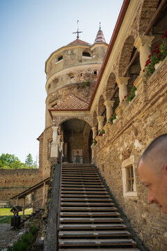 View of ancient stone steps leading up to a majestic tower, framed by arched walkways adorned with vibrant flowers, in Cris, Transilvania, Romania.