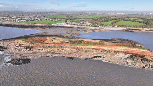 Aerial view of the rugged Sully Island coastline where the reddish-brown cliffs meet the grey, turbulent sea, Sully Island, Wales, United Kingdom.