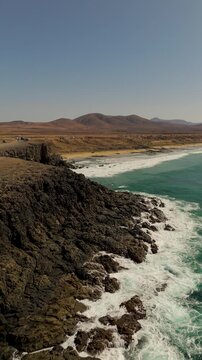 Vertical Drone Approach Shot of Playa del Castillo, a stunning white sand beach contrasting with turquoise Atlantic Ocean water near El Cotillo, Fuerteventura, Canary Islands.