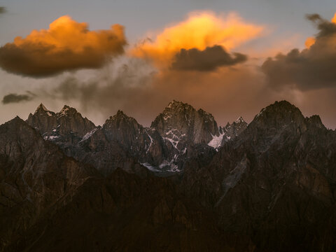 View of jagged, snow-touched peaks thrust skyward beneath a dramatic, golden-tinged cloudscape, evoking a sense of awe and the raw beauty of nature, Khaplu, Gilgit Baltistan, Pakistan.