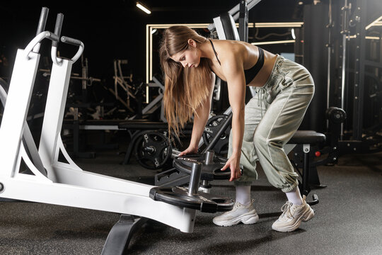 Female athlete loading weight plates on strength machine in gym preparing for workout