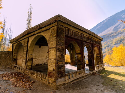 View of an aged, open-air pavilion with arched openings stands in the foreground, backed by golden autumn trees and steep mountain slopes, Hopar, Gilgit Baltistan, Pakistan.