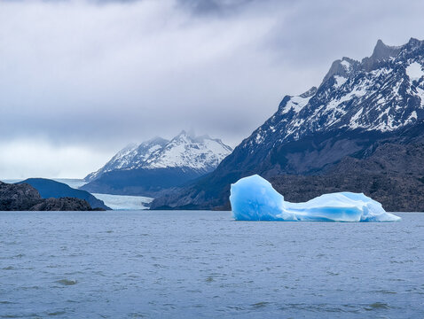 Eine gro&szlig;e Eisscholle treibt auf dem Grey Lake in Patagonien, Chile im Hintergrund einige Berge