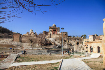 View of ancient temple complex with weathered stone walls and intricate carvings under a clear blue sky, a silent testament to history, Katas, Punjab, Pakistan.