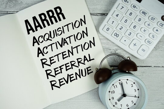 AARRR Acquisition, Activation, Retention, Referral, Revenue text on paper notebook page with alarm clock and calculator on wooden background