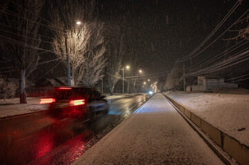Winter cityscape with snowfall and car on road in motion