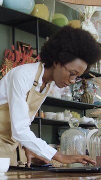 Splendid busy concentrated experienced 25-30-aged black-skinned female souvenirs shop's keeper doing photos of different things and uploading pictures on laptop for online shop website slow motion