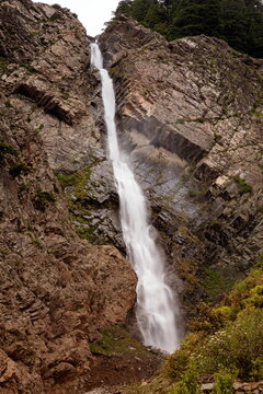 View of a powerful waterfall cascading down rugged, rocky cliffs, framed by sparse vegetation, creating a dramatic and serene scene, Kalam, Khyber Pakhtunkhwa, Pakistan.