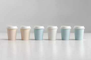 Collection of paper coffee cups in different colors arranged on a table against a plain background