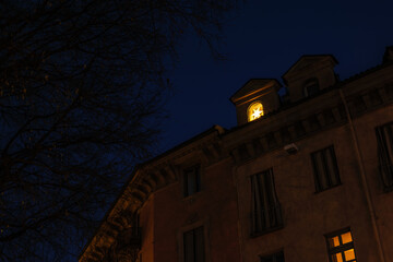 Turin, Italy. Evening view of a historic building facade in Largo IV Marzo, with a warmly lit window glowing with a Christmas star against the deep blue sky of the city.