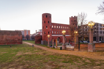 Turin, Italy. View from the Palatine Towers Archaeological Park of Porta Palatina, the ancient Roman gate of Turin, with brick towers, arches, walls, and open green space at dusk. 