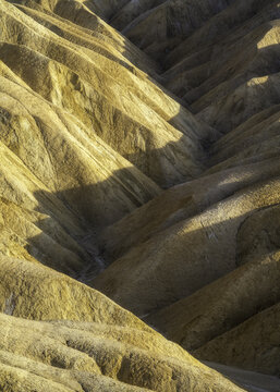 View of layered, golden earth undulates in soft light, casting long shadows across the arid landscape, revealing textures and tones, Death Valley, California, United States.