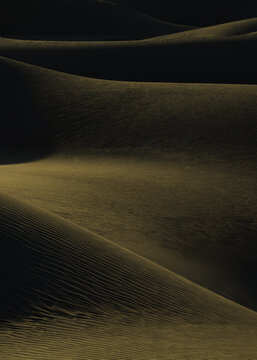 View of golden sand dunes cascade in rippling waves under stark shadows, creating an abstract landscape of texture and form, Death Valley, California, United States.