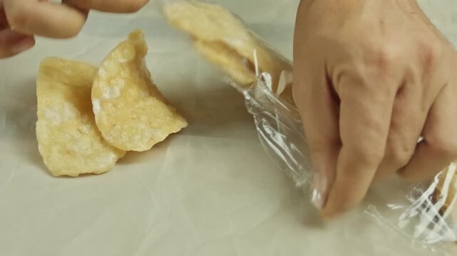 Hands opening plastic packaging then breaking crispy sweet crackers and placing them on a clean white table surface