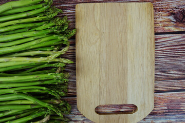 Bunch of fresh green asparagus stems with cutting wooden board on wooden background