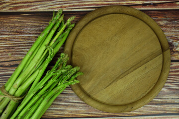 Bunch of fresh green asparagus stems with cutting wooden board on wooden background