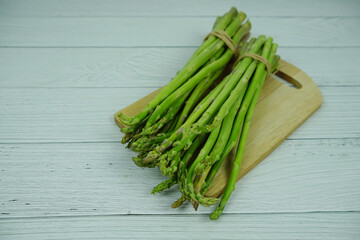 Bunch of fresh green asparagus stems with cutting wooden board on wooden background