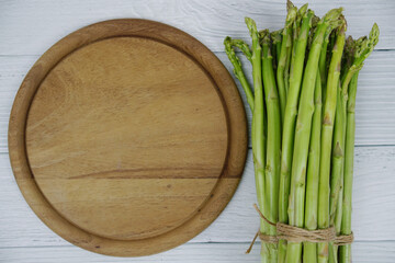 Bunch of fresh green asparagus stems with cutting wooden board on wooden background