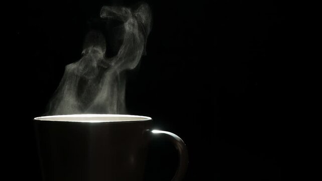 Mug of Hot Coffee. A trickle of steam rises and twists gracefully from a cup of hot Coffee. Backlight illuminates brown cup on a black background