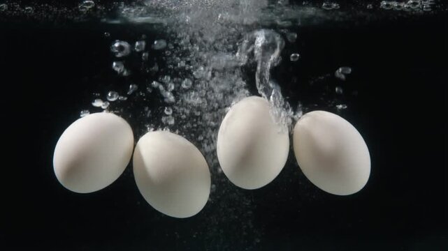 Four white eggs boiling in water with rising bubbles against a dark background.