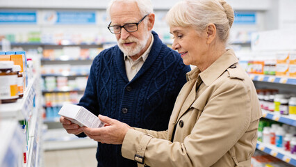 An elderly couple in coats stands in a pharmacy aisle, carefully reading the information on a medicine box together before making a purchase