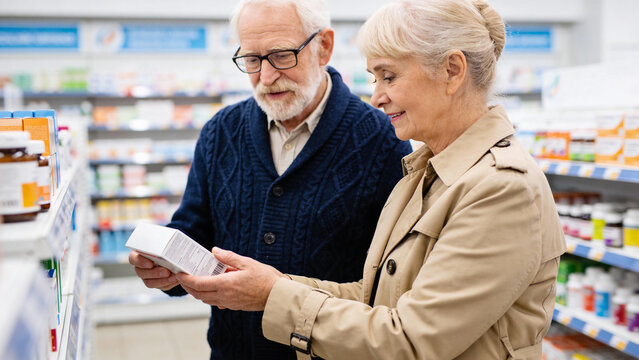An elderly couple in coats stands in a pharmacy aisle, carefully reading the information on a medicine box together before making a purchase - Powered by Adobe