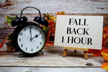 Fall Back 1 Hour text with alarm clock and maple leaf decoration on wooden background