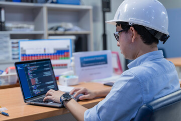 Asian male engineer wearing hardhat coding on laptop in industrial office. Professional technician...