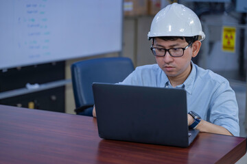 Asian male engineer wearing hardhat coding on laptop in industrial office. Professional technician...