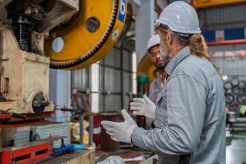 Industrial engineers wearing safety gear inspecting heavy machinery in a modern factory. Factory...